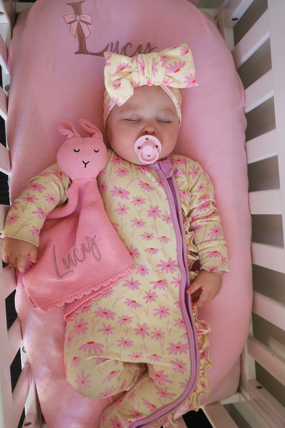 Personalised knitted baby blanket with embroidered name, shown with a sleeping baby and matching pink bunny comforter