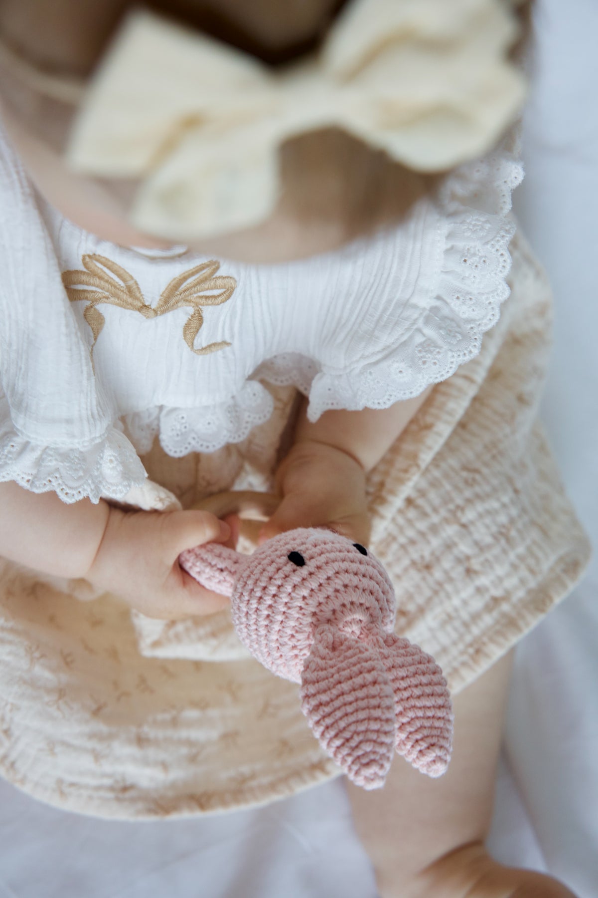 Baby holding a pink crochet bunny teether with natural wooden ring