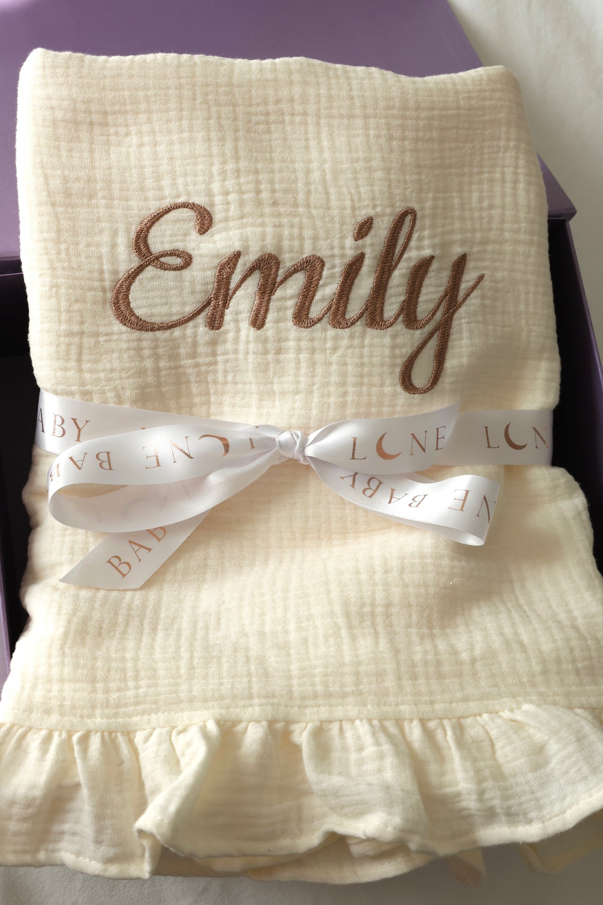 Personalised muslin baby blanket with embroidered name and ruffled edge, gift wrapped with Lune Baby ribbon