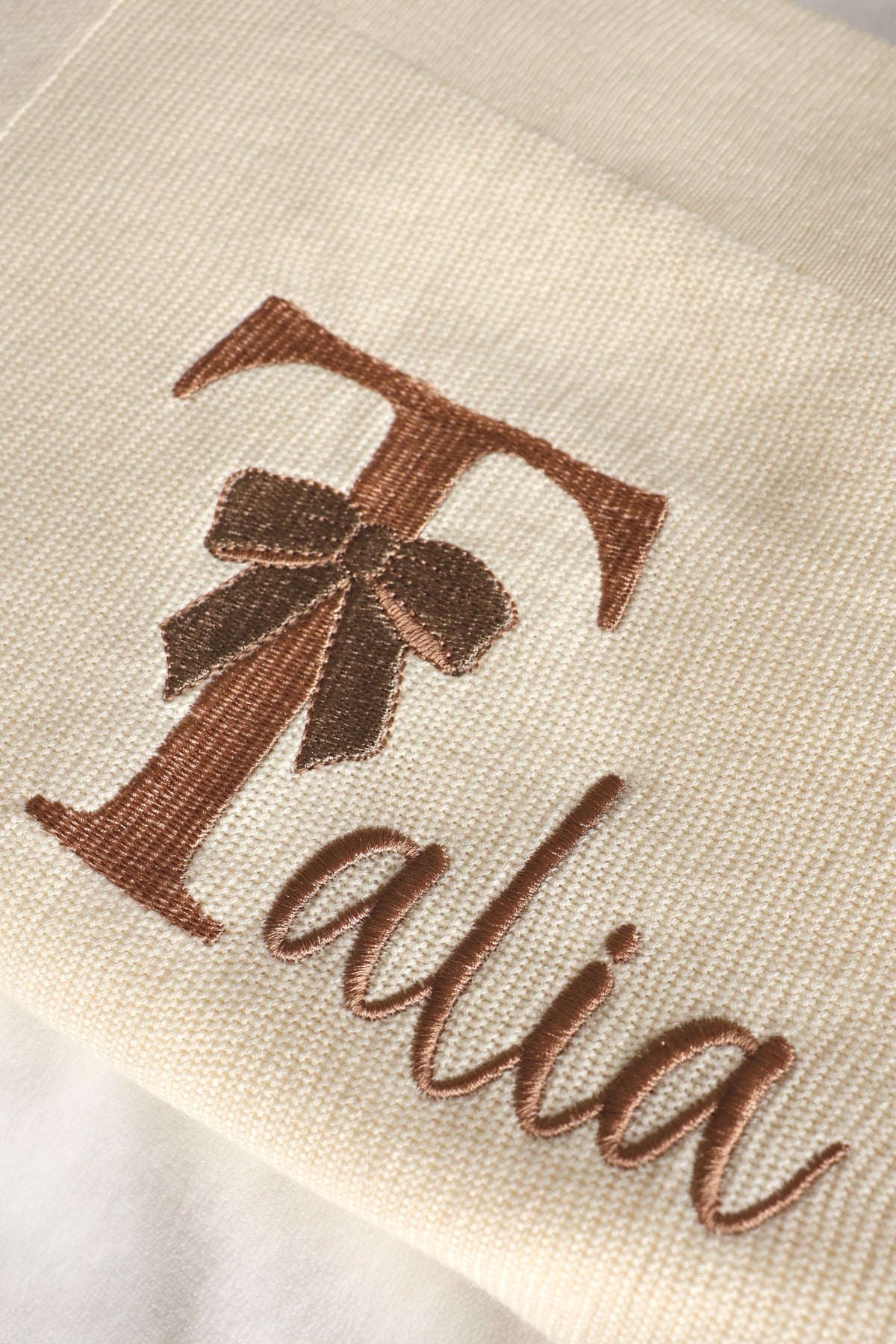 Close-up of personalised knitted cotton baby blanket with embroidered name and bow design